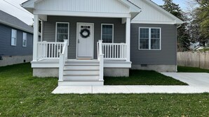 Ein zweistöckiges Haus mit Veranda, Haustür und einem Kranz sowie einem kleinen Vorgarten.