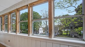 A room with large windows, wooden frames, and a white paneled wall.