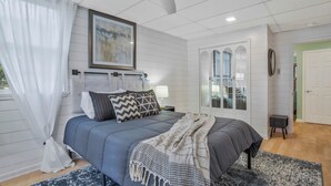 A bedroom with a bed, a ceiling fan, a nightstand with a lamp, and a door leading to another room.