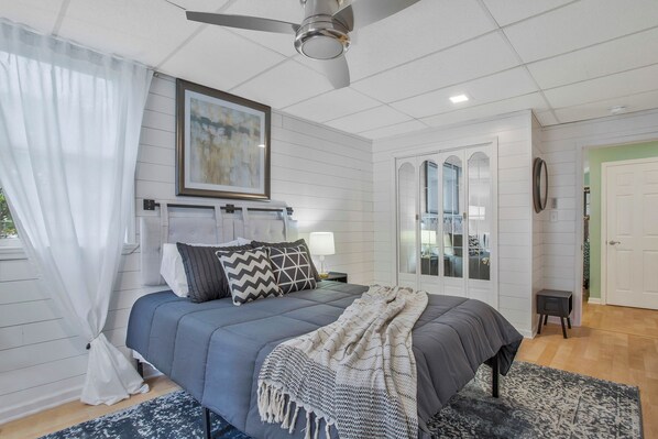 Een slaapkamer met een bed, een plafondventilator, een nachtkastje met een lamp, en een deur naar een andere kamer.