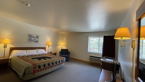 A hotel room with a bed, two bedside lamps, a chair, a desk with a computer, and a window with curtains. - AuSable Valley Inn (Mio)