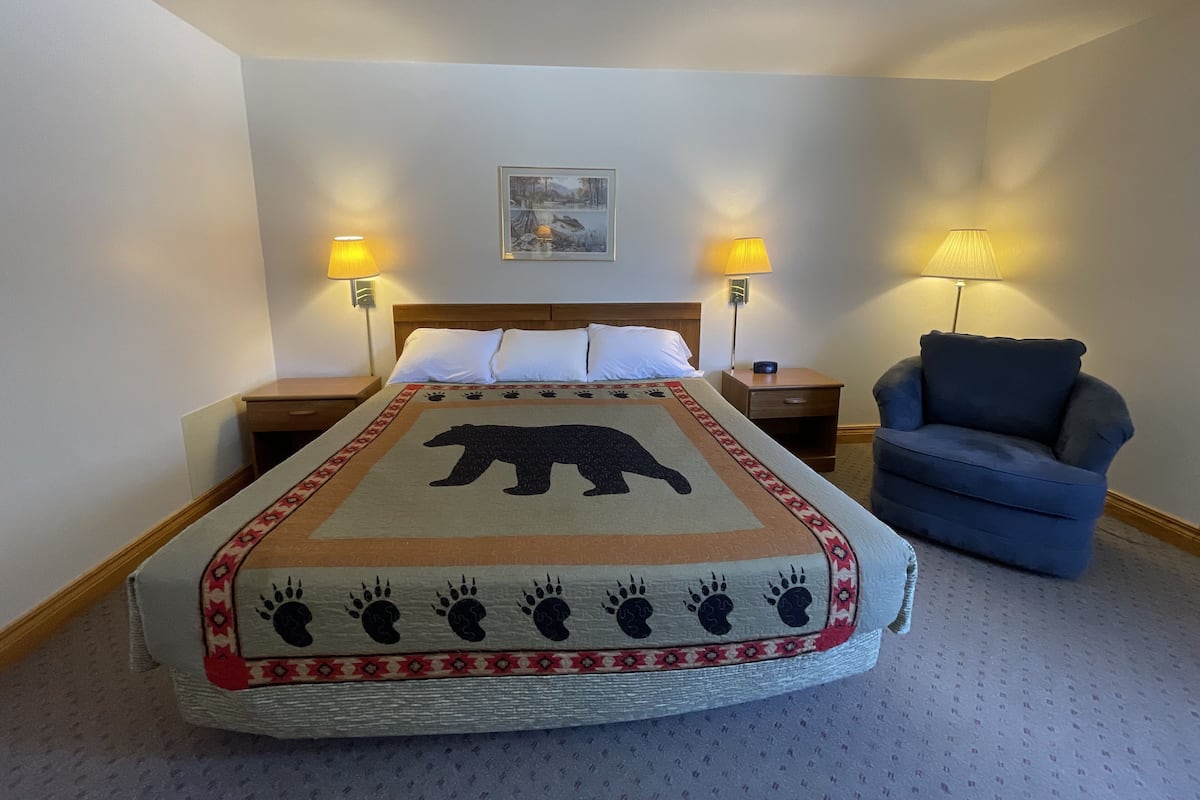 A hotel room with a bed, two bedside lamps, a chair, and a painting on the wall.
