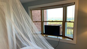 A bedroom with a bed, a window with a view of a building and a body of water, and a television on a stand. - Attached Apartment Near It All. Organic Farmstead. Stunning Views. Pet-friendly. (New Shoreham)