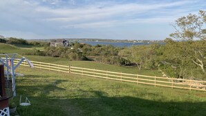 A grassy area with a wooden fence, a white chair, and a table. - Attached Apartment Near It All. Organic Farmstead. Stunning Views. Pet-friendly. (New Shoreham)