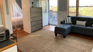 A bedroom with a bed, a grey wardrobe, a grey sofa, and a large window. - Attached Apartment Near It All. Organic Farmstead. Stunning Views. Pet-friendly. (New Shoreham)