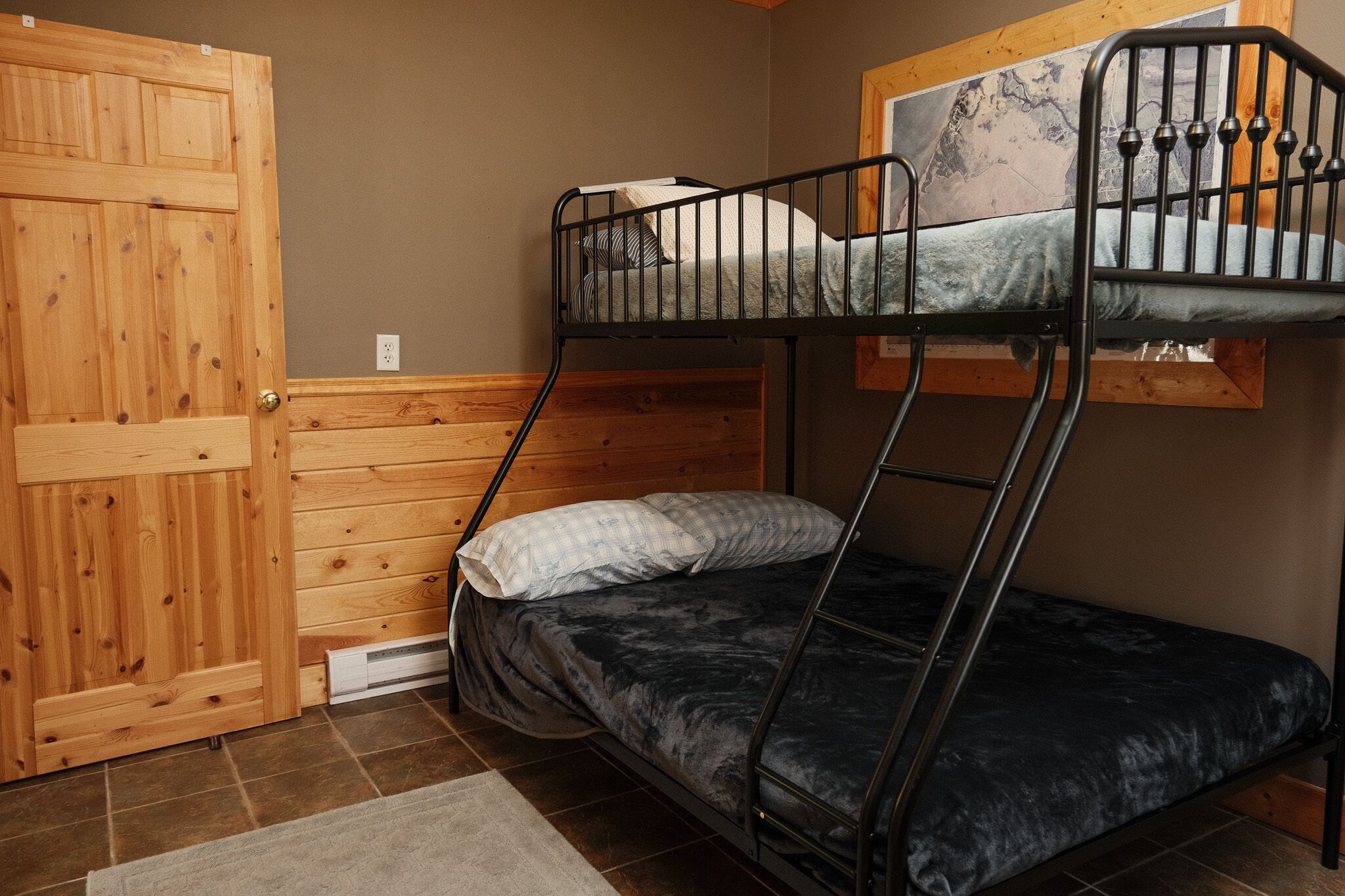A bunk bed room with a wooden door, a window with a view, and a tiled floor.