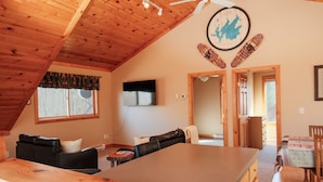A cozy, wooden-floored living room with a large table, a sofa, and a TV mounted on the wall. - Welcome to Leech Lake Lodge! (Federal Dam)