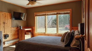 A bedroom with a large window, wooden walls, a bed, a TV, and a wooden cabinet. - Welcome to Leech Lake Lodge! (Federal Dam)