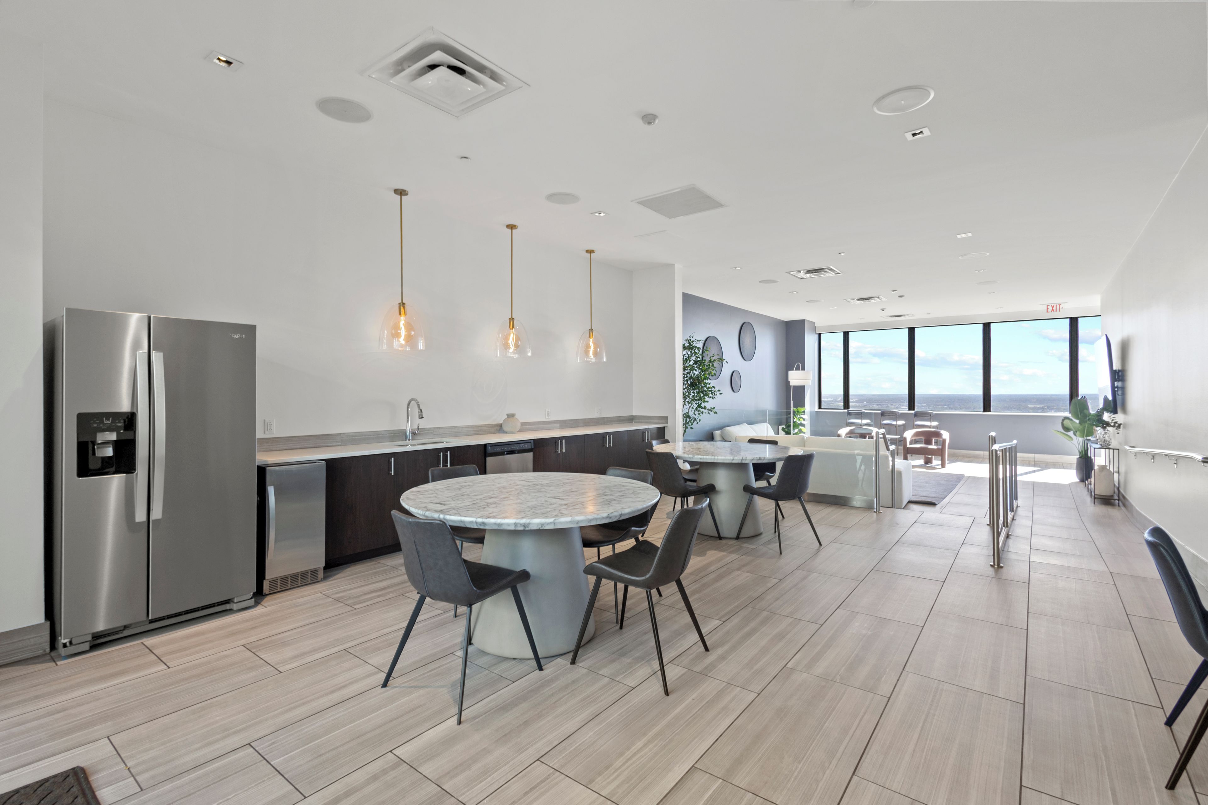A modern kitchen with a stainless steel refrigerator, a marble island, and pendant lighting.