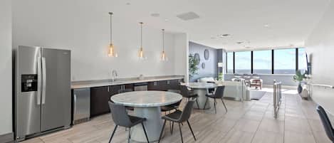 A modern kitchen with a stainless steel refrigerator, a marble island, and pendant lighting.