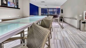 A modern indoor pool area with glass tables and wicker chairs, large windows, and a city view. - Luxury Apt In City Heart with Pool Gym & PoolTable (Dallas)