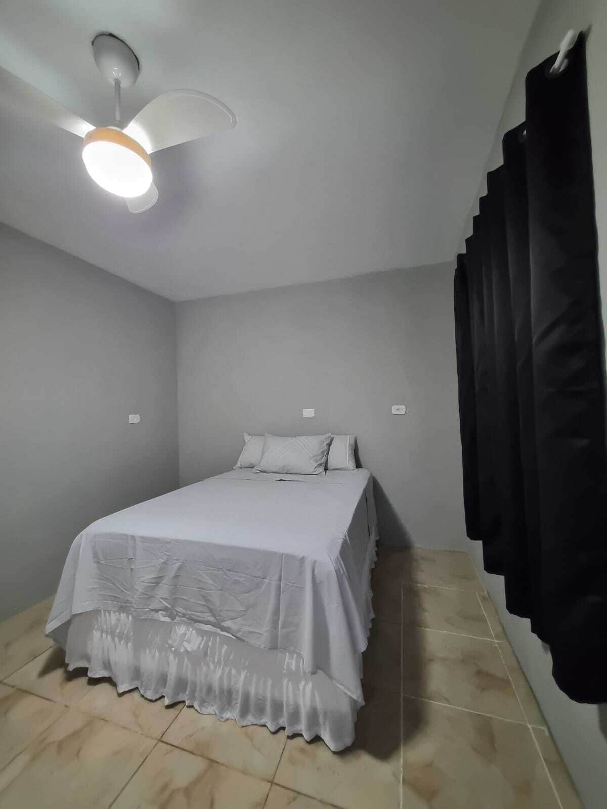Un dormitorio con cama, ventilador de techo y cortina negra.