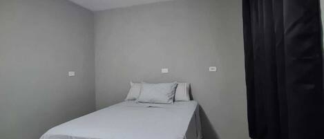 Un dormitorio con cama, ventilador de techo y cortina negra.