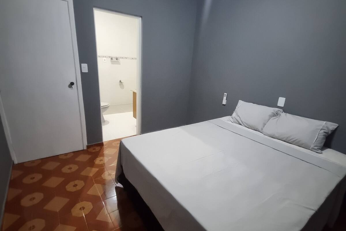 Een slaapkamer met een bed, een deur en een zichtbare badkamer door een open deur.