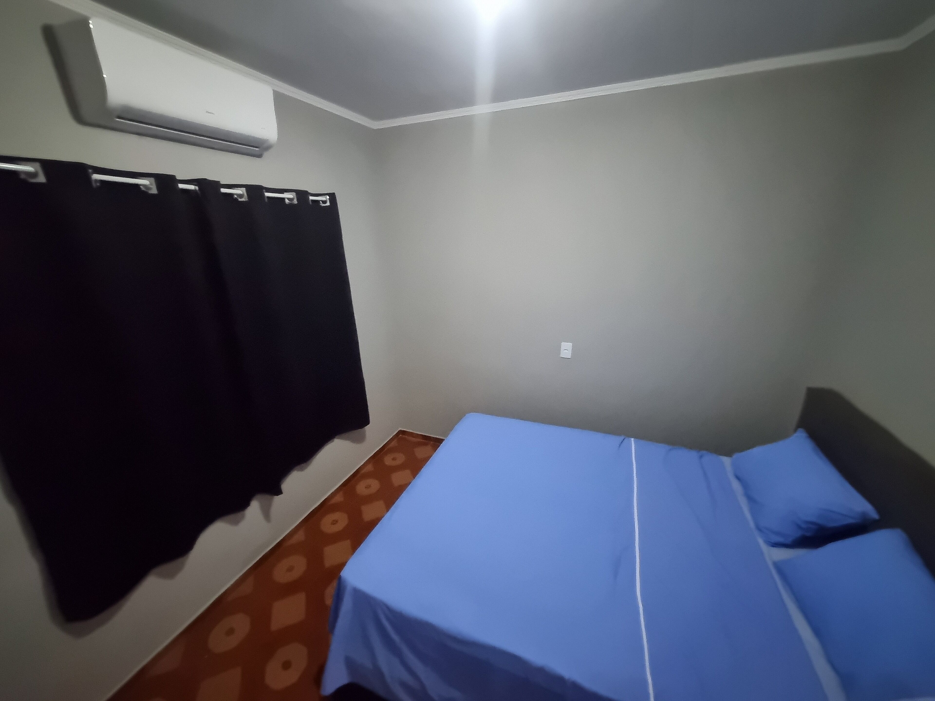 A room with a bed, a wall-mounted air conditioner, and a patterned floor.
