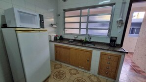 A kitchen with a white refrigerator, a microwave on top, a window with blinds, and patterned floor tiles.