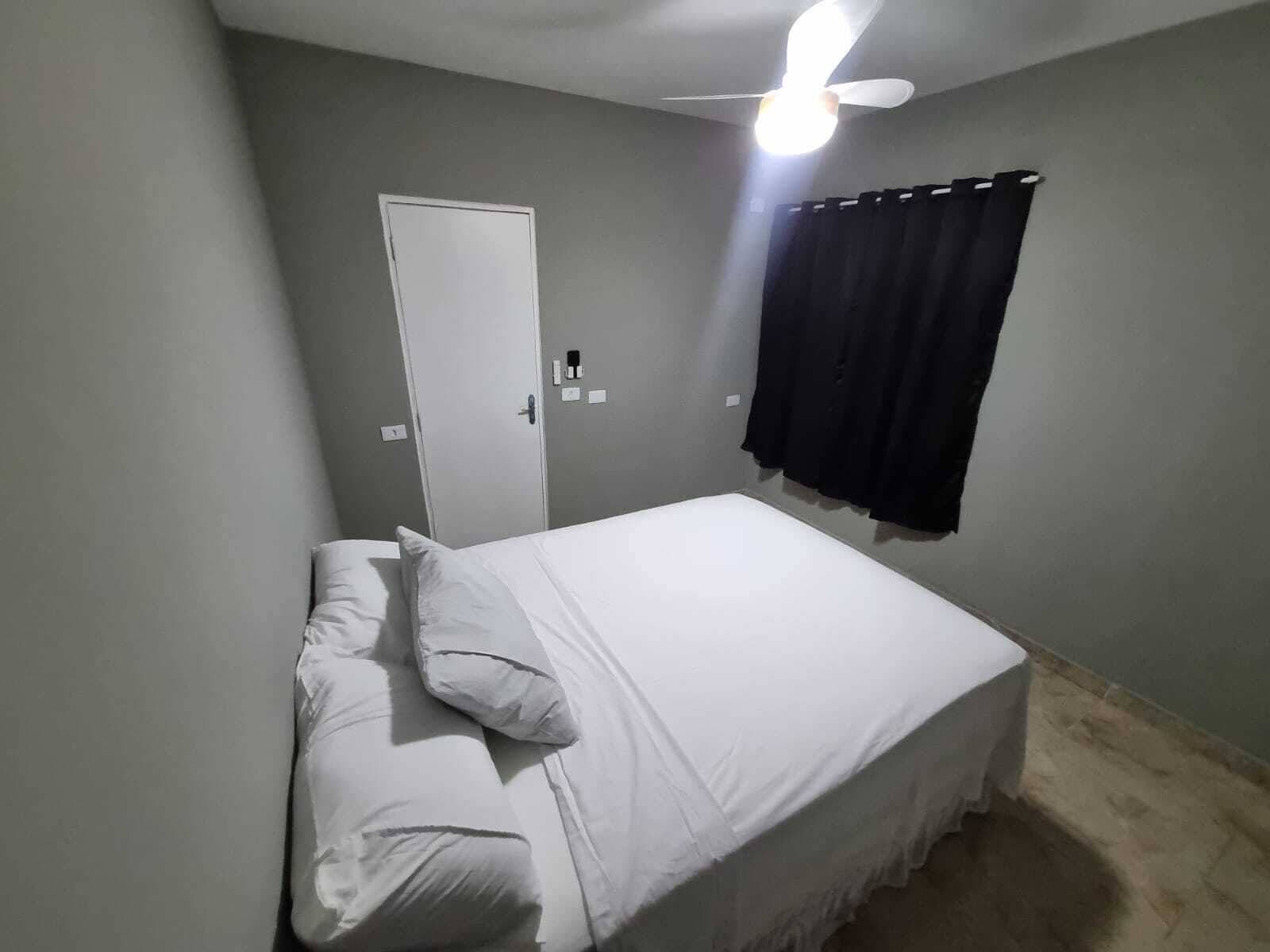 Quarto com cama, ventilador de teto, porta e janela com cortinas.