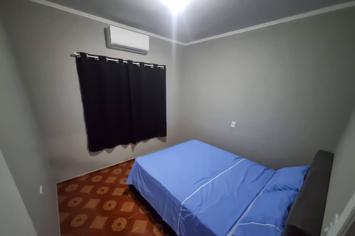 Een kleine kamer met een enkel bed, een blauw sprei, een zwart gordijn en een vloer met een patroon.
