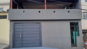 A modern two-story building with a grey facade, a large garage door, and a small window with metal bars.