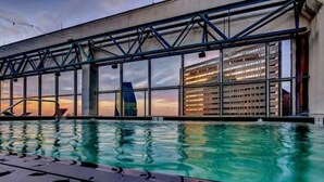 A swimming pool with a modern architectural backdrop, large windows, and a clear view of the sky. - Luxury 1 Bhk Apt w/Parking Pool / Gym/ City View (Dallas)