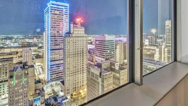 A nighttime cityscape viewed from a high-rise building with illuminated windows and a prominent building with a red light on top. - Luxury 1 Bhk Apt w/Parking Pool / Gym/ City View (Dallas)