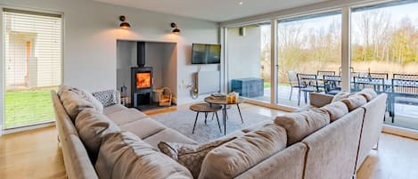 A modern living room with a large sectional sofa, a fireplace, a flat-screen TV, and a dining area with outdoor seating.