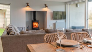 A cozy living room with a sofa, a table set for dining, a fireplace, and a TV mounted on the wall.