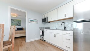 Una cocina moderna con gabinetes blancos, electrodomésticos de acero inoxidable y piso de madera en patrón de espiga.