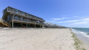 Un hotel frente a la playa con varios balcones, una terraza de madera y un muelle que se adentra en el agua.