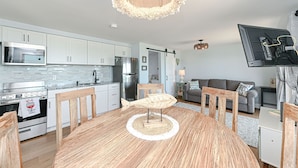 Una cocina moderna con armarios blancos, electrodomésticos de acero inoxidable y un comedor con mesa y sillas de madera.