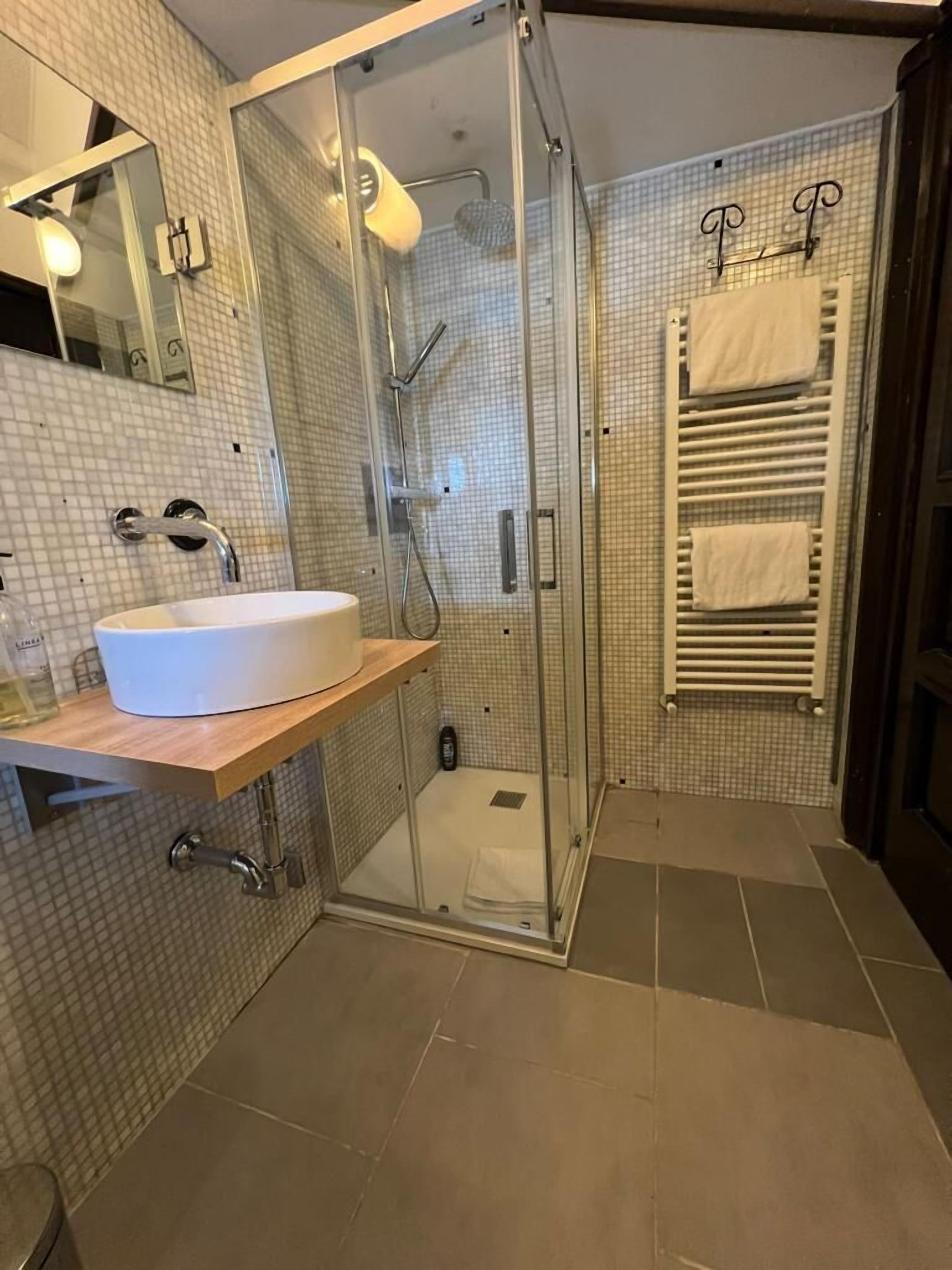 Un bagno moderno con doccia vetrata, lavandino bianco e porta asciugamani.