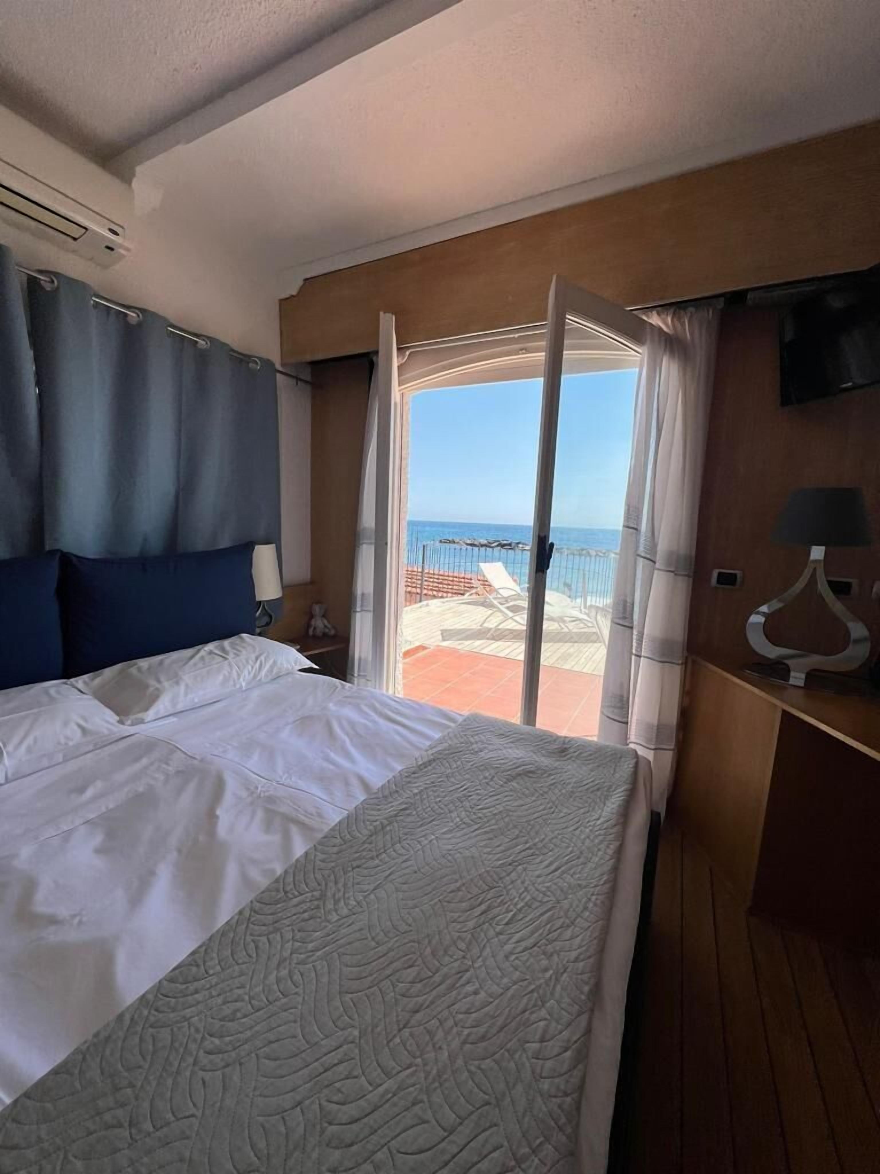 A hotel room with a bed, a TV, and a view of the beach.