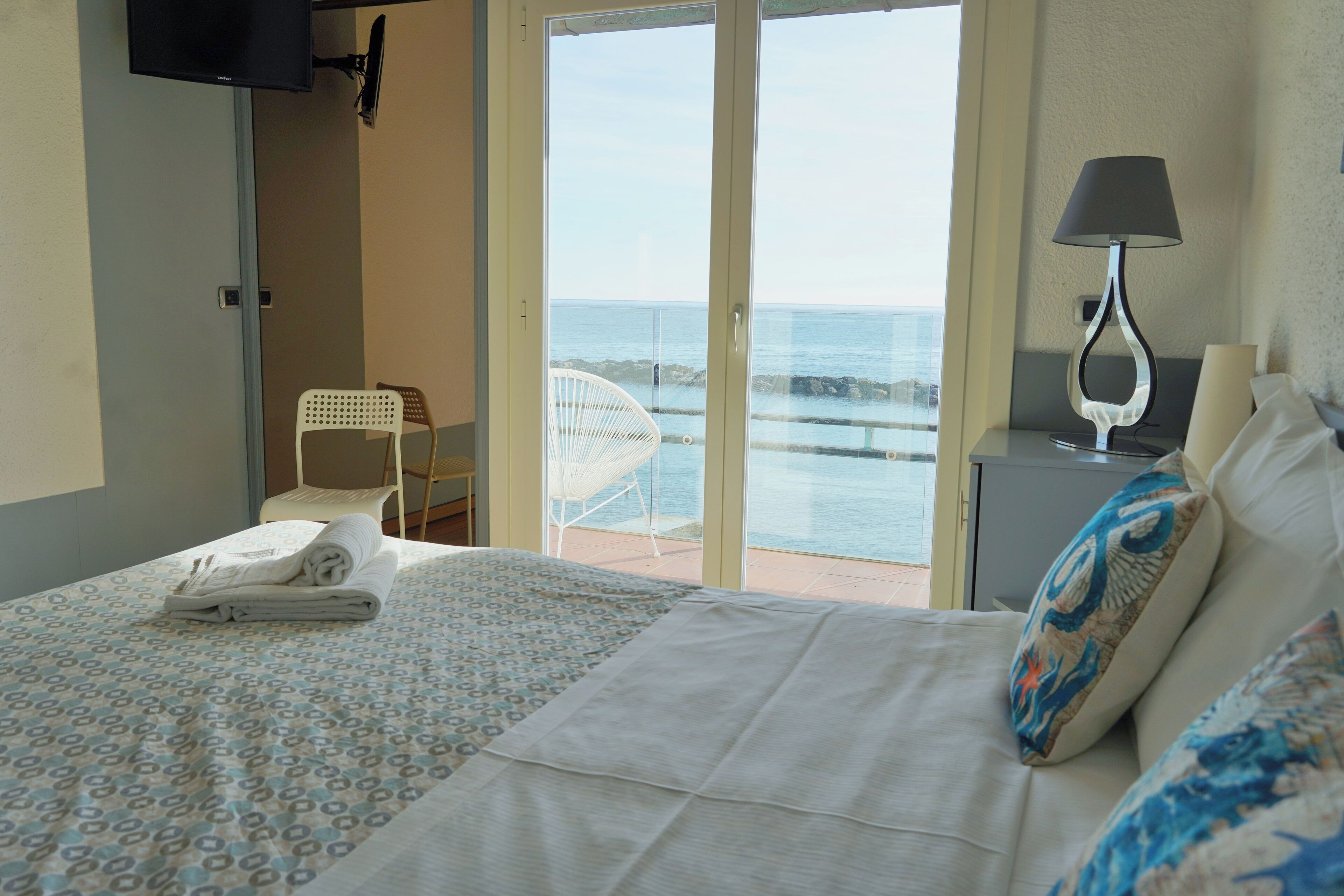 Una habitación de hotel con cama, una silla, una mesita de noche, una lámpara y un televisor.