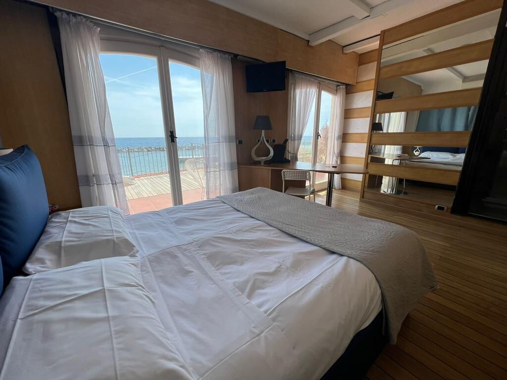 Une chambre avec un grand lit, un bureau et une vue sur la mer.