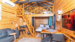 A cozy cabin interior with a loft bedroom, a sofa, a dining area, and a TV. - AYVALIK TRİNGO BUNGALOV (Ayvalik)
