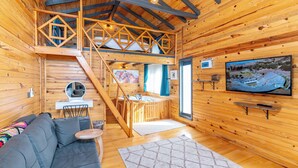 A cozy cabin interior with a wooden interior, a sofa, a desk, a bathroom, and a TV displaying a scenic view. - AYVALIK TRİNGO BUNGALOV (Ayvalik)