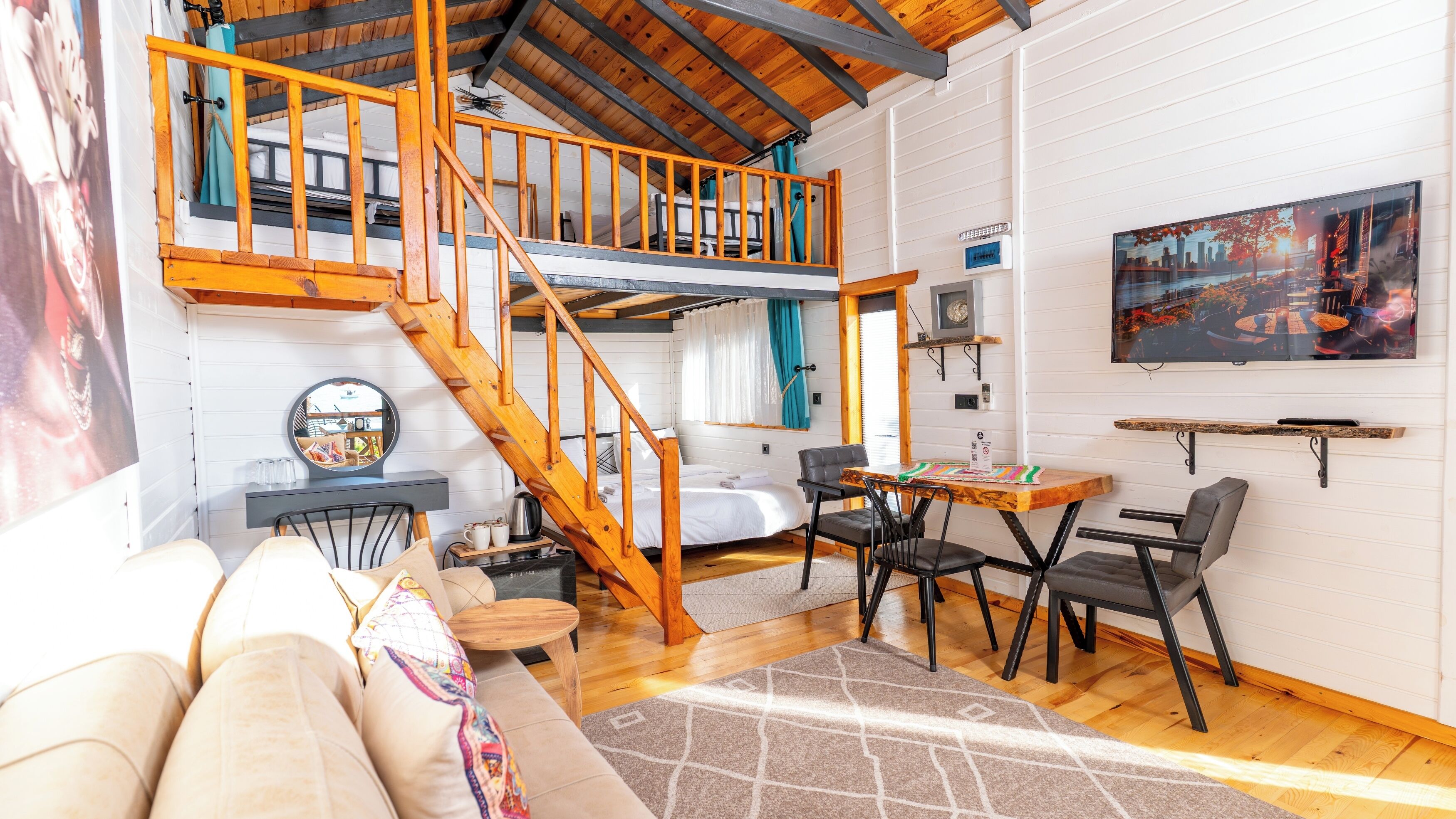 A cozy loft-style room with a wooden staircase, a dining area, and a large window with a cityscape view.