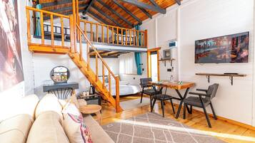 A cozy loft-style room with a wooden staircase, a dining area, and a large window with a cityscape view.
