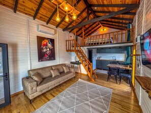 A cozy cabin interior with a loft bedroom, a dining area, and a living room with a sofa and a rug. - AYVALIK TRİNGO BUNGALOV (Ayvalik)