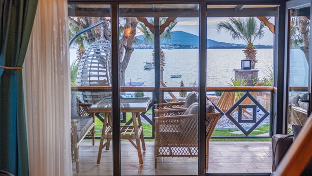 A balcony with wicker furniture, a hammock, and a view of the sea with boats. - AYVALIK TRİNGO BUNGALOV (Ayvalik)