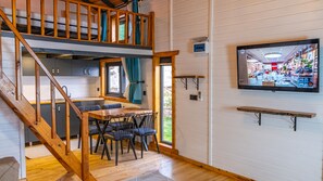 A multi-level wooden interior with a dining area, kitchen, and a TV displaying a store interior. - AYVALIK TRİNGO BUNGALOV (Ayvalik)