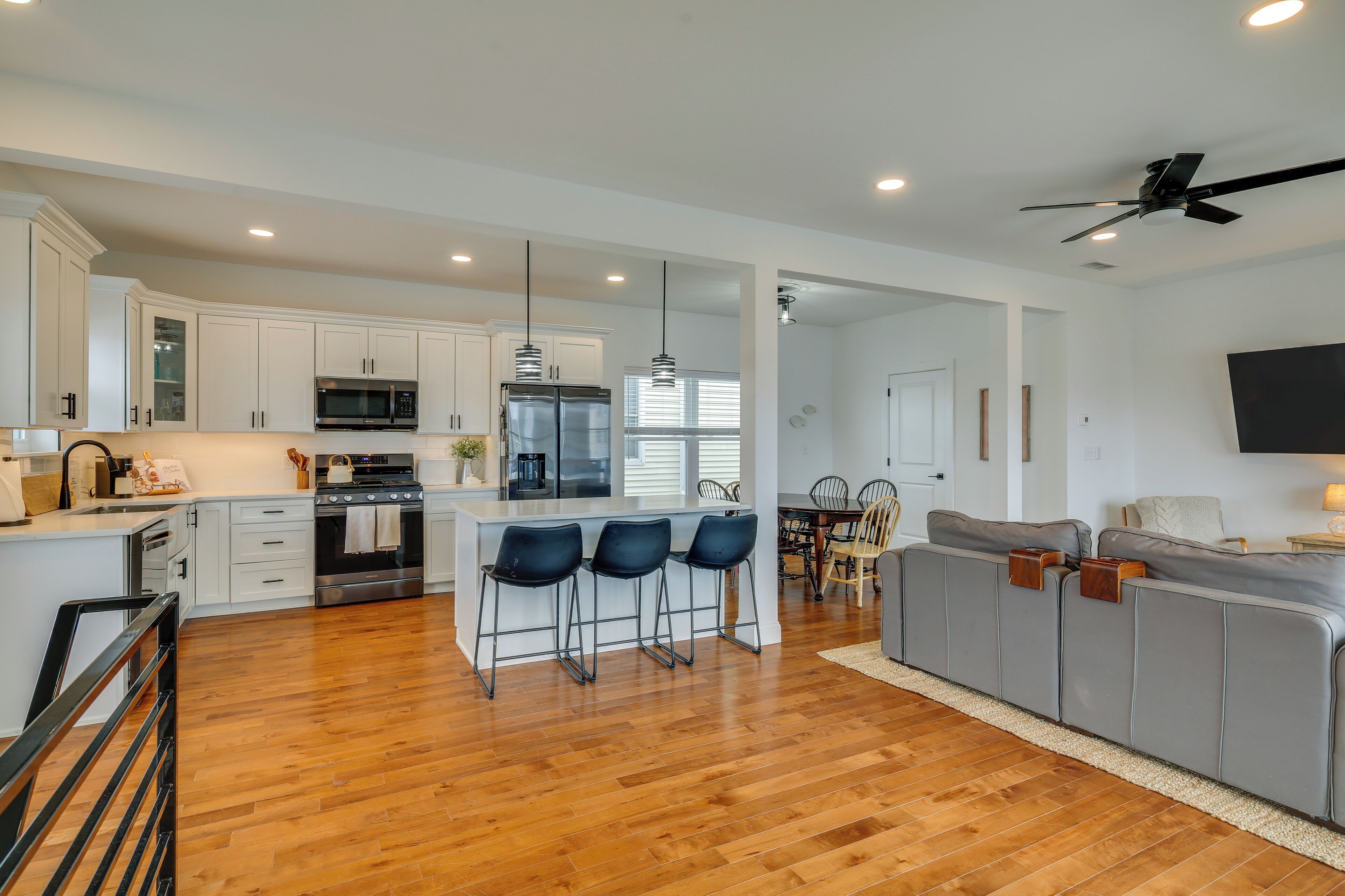 A modern kitchen with white cabinets, stainless steel appliances, and a bar area with black bar stools.