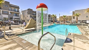 Piscina com um elemento aquático, rodeada por edifícios modernos e palmeiras.