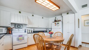 A kitchen with white cabinets, a wooden dining table with chairs, a refrigerator, and a microwave. - House on Paw Paw Lake w/ Private Dock! (Watervliet)