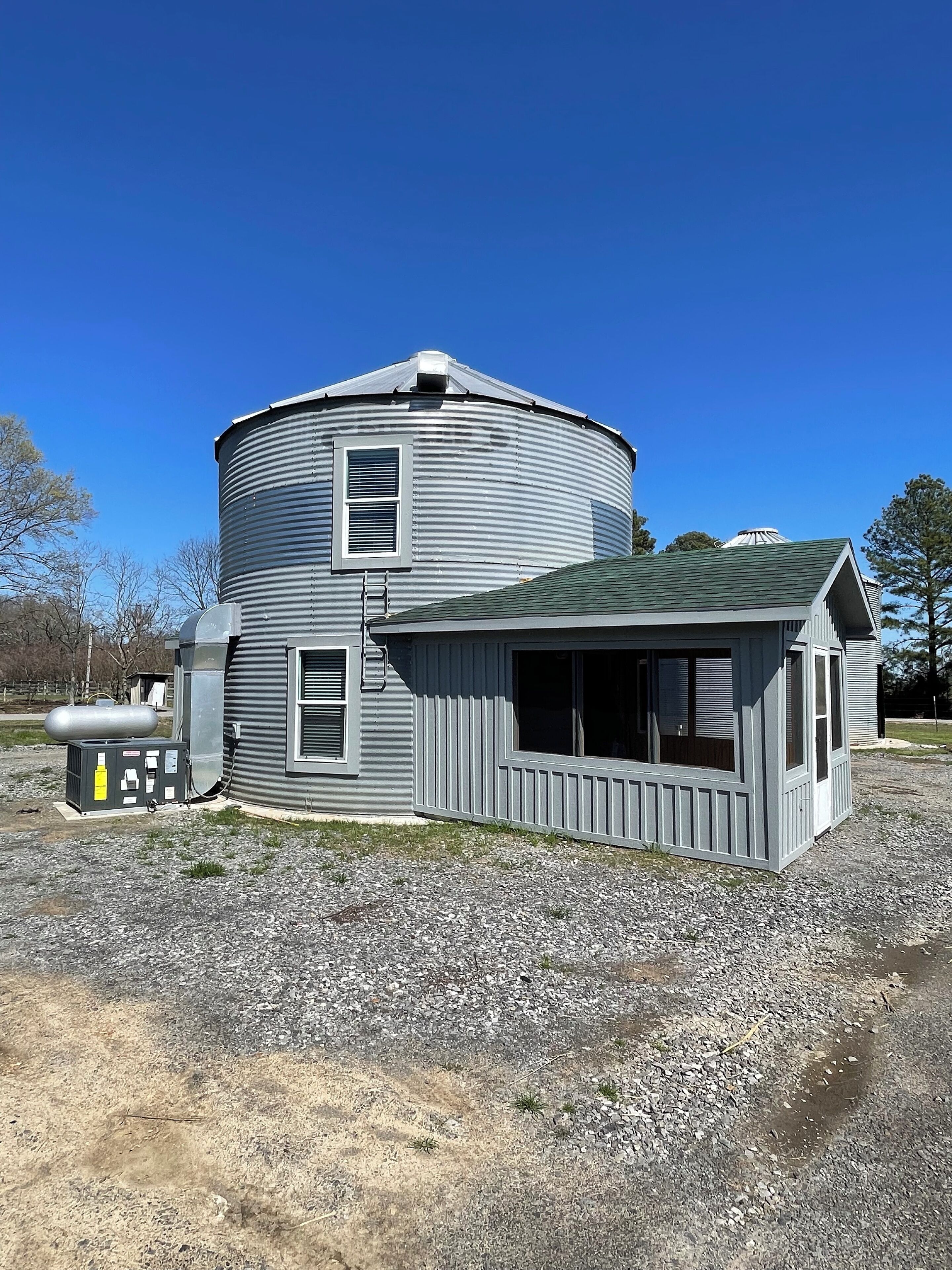 A large, cylindrical grain silo with a small attached building featuring large windows and a sloped roof.