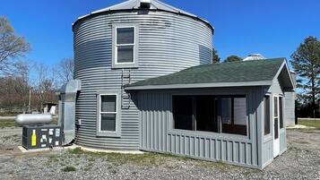 A large, cylindrical grain silo with a small attached building featuring large windows and a sloped roof.