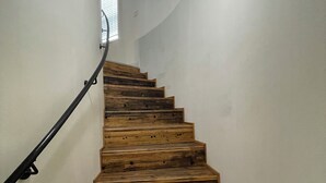 Una escalera de madera con barandilla negra que sube hacia una ventana con persianas.