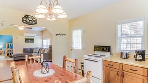 Una cocina acogedora con una mesa de comedor de madera, sillas y una estufa. Se ve un sofá y una pequeña mesa de comedor al fondo.