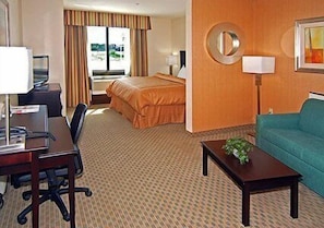 A hotel room with a bed, a desk with a chair, a sofa, a coffee table, a lamp, and a window with curtains. - Fairfield Inn & Suites Hillsboro (Hillsboro)
