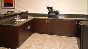 A kitchen with dark wooden cabinets, a granite countertop, a sink, and a microwave. - Fairfield Inn & Suites Hillsboro (Hillsboro)